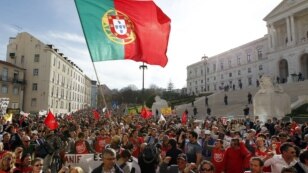 Demonstrators wave a Portuguese flag and shout slogans outside the parliament, at right, during a workers protest, Lisbon, Thursday, March 22, 2012.